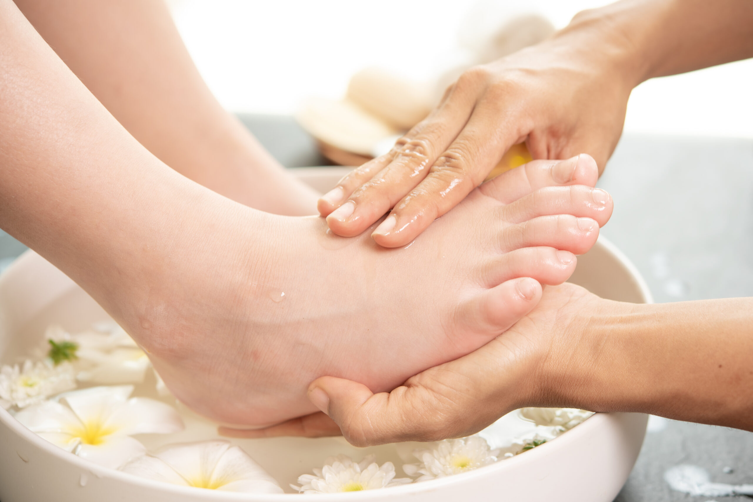foot washing in spa before treatment. spa treatment and product foot washing in spa before treatment. spa treatment and product for female feet and hand spa. white flowers in ceramic bowl with water for aromatherapy at spa.
