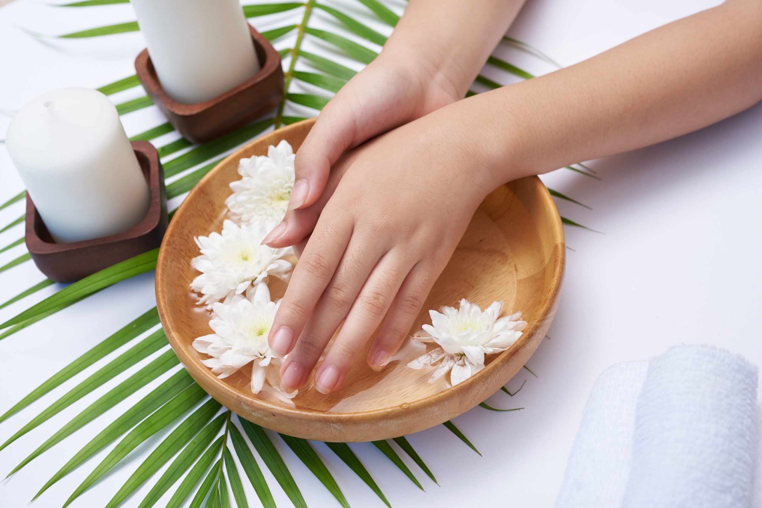 Woman soaking her hands in bowl of water and flowers, Spa treatm Woman soaking her hands in bowl of water and flowers, Spa treatment and product for female feet and hand spa, massage pebble, perfumed flowers water and candles, Relaxation. Flat lay. top view.